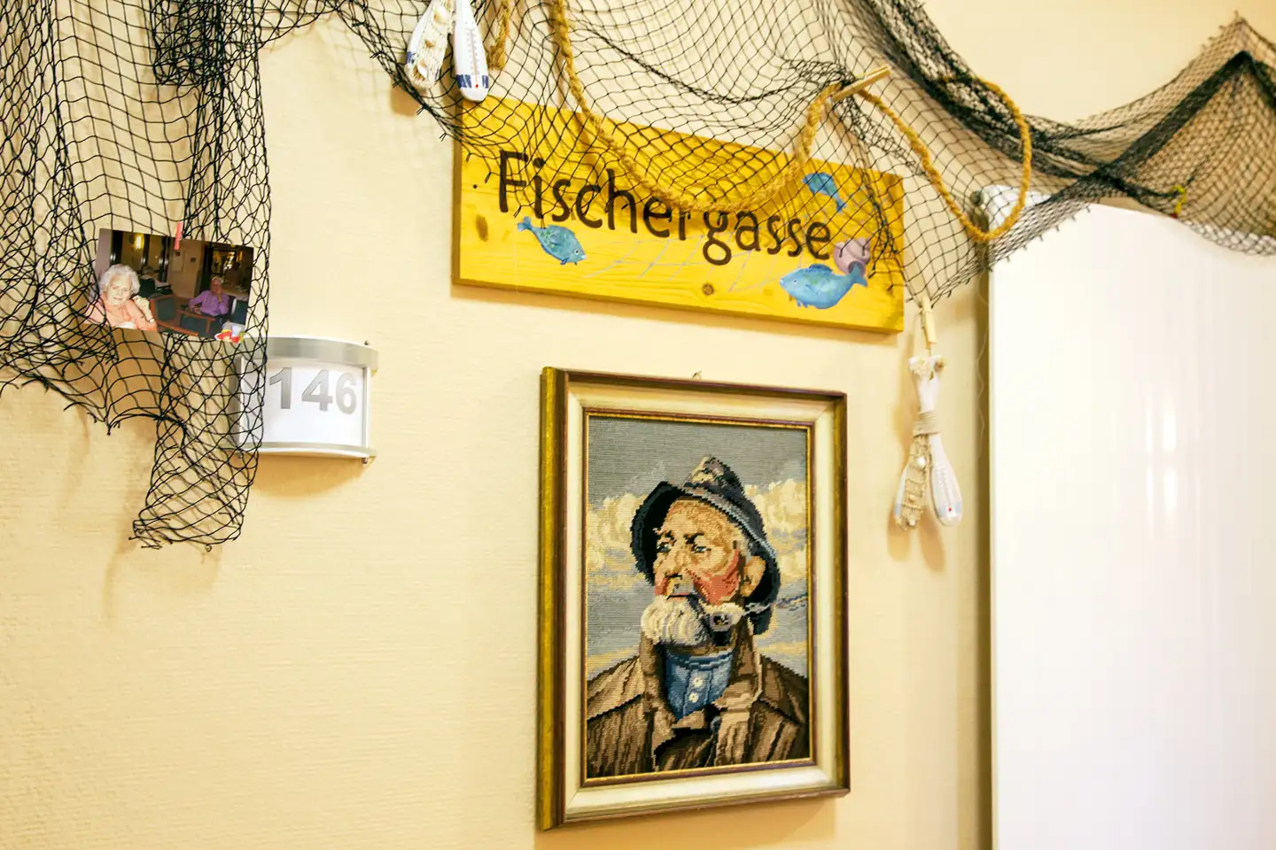 Wand mit maritimem Stickbild und Schild "Fischergasse"